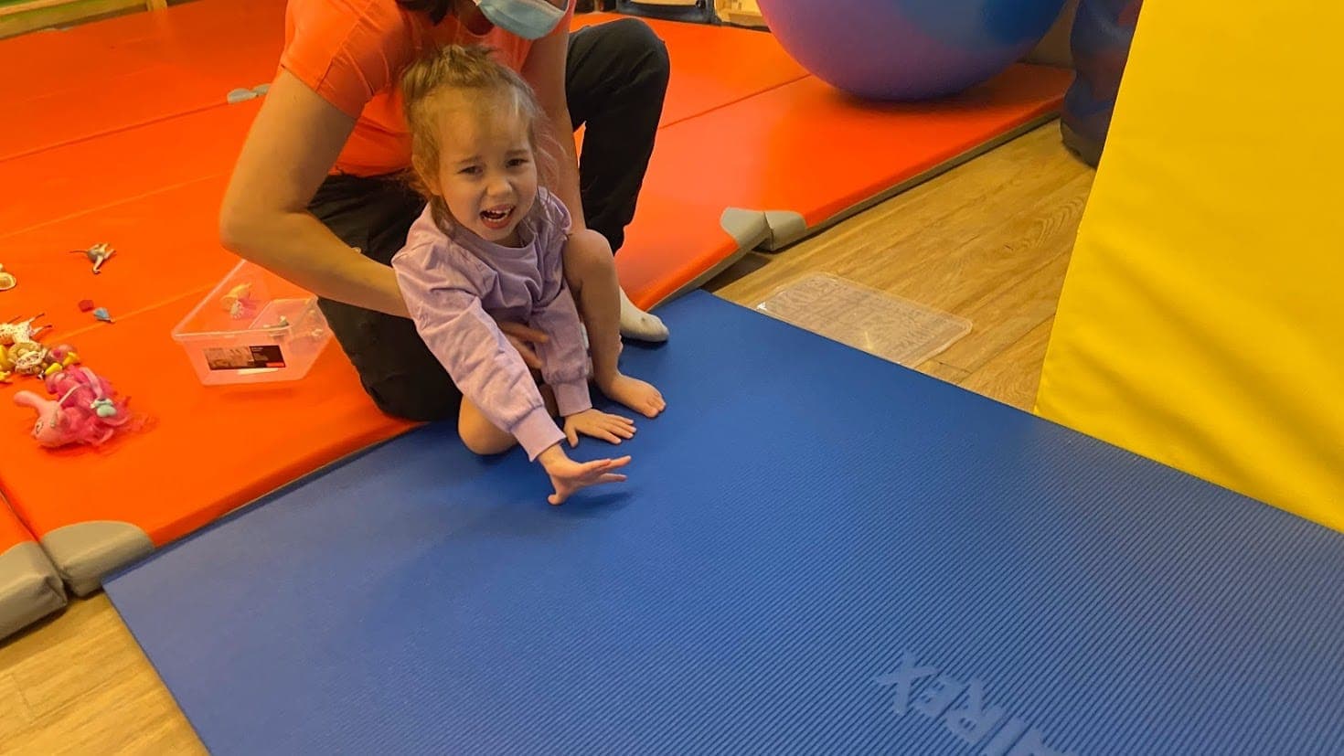 Maryla siedzi na niebieskiej macie w sali terapeutycznej